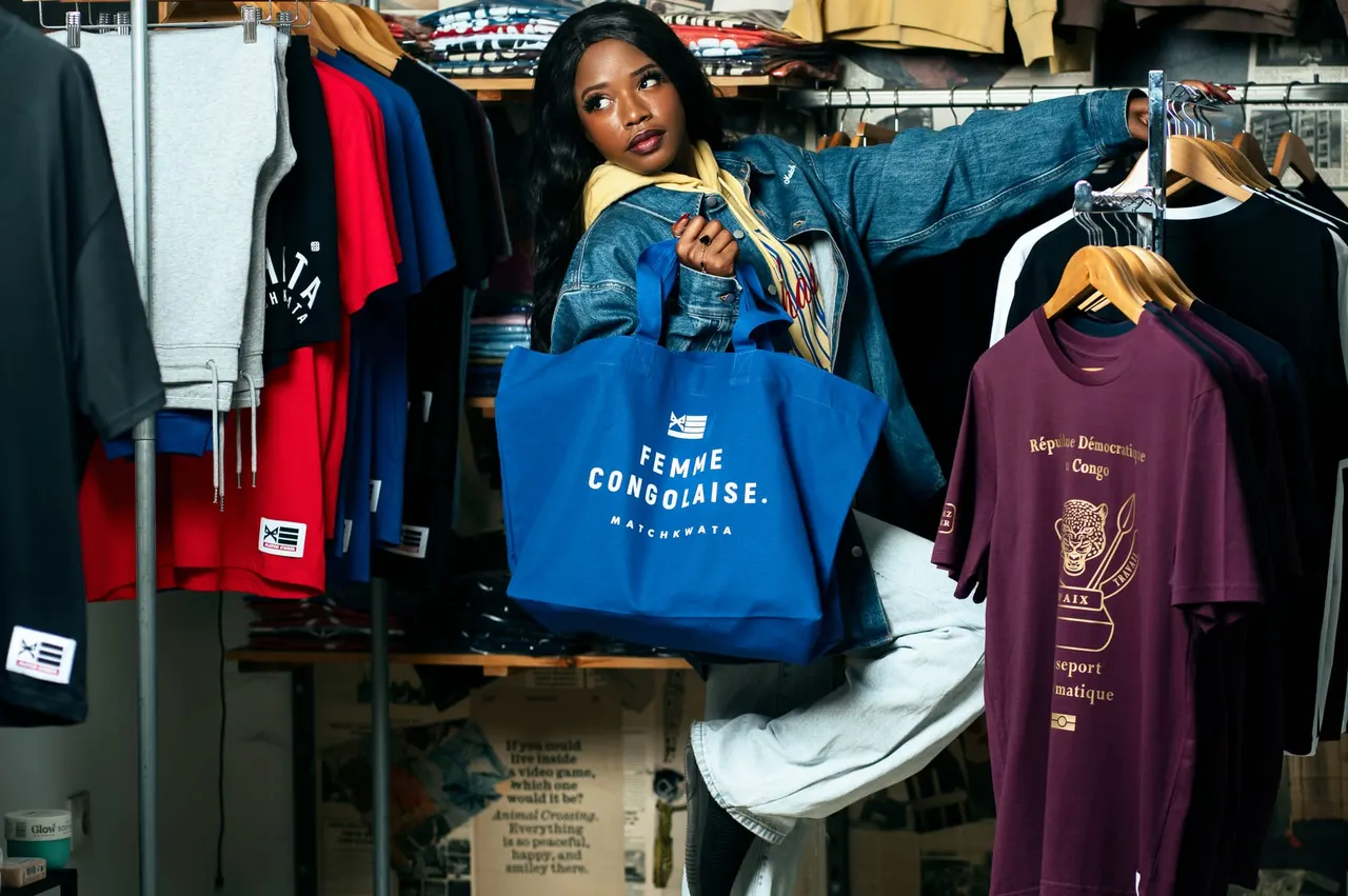 Une cliente en veste en jean, tote bag Match Kwata à la main, devant les portants de la boutique