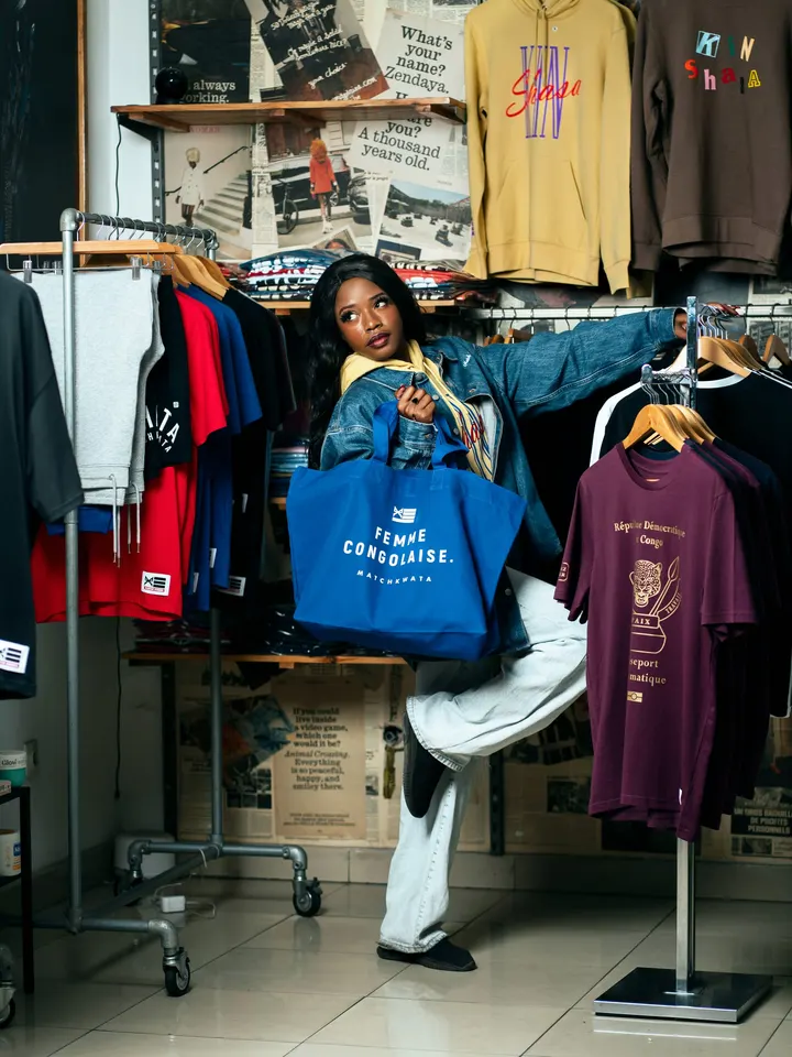Une cliente en veste en jean, tote bag Match Kwata à la main, devant les portants de la boutique